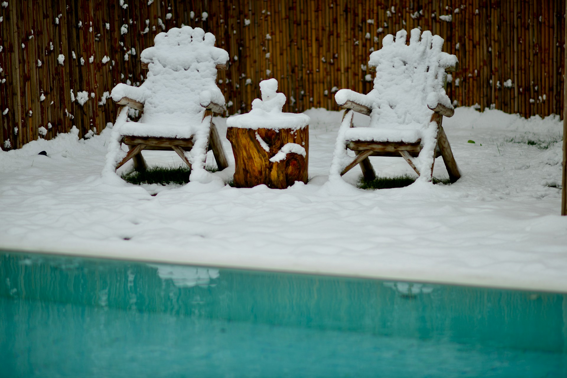 two lawn chairs covered in snow next to a pool